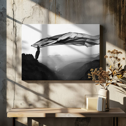 A dramatic black and white photograph of a woman standing on the edge of a mountain peak. She holds up a massive piece of dark, sheer fabric that billows in the wind, stretching across the sky. Below her, a vast, misty mountain range and a deep valley with city lights are visible. Wall Art