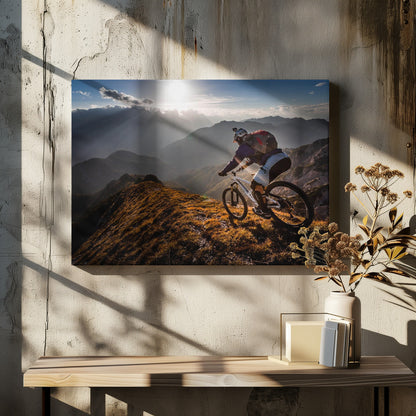 A mountain biker navigates a narrow, golden-lit ridge against a backdrop of a vast mountain range. The sun is breaking through clouds in the distance, casting dramatic rays of light across the epic landscape. Print