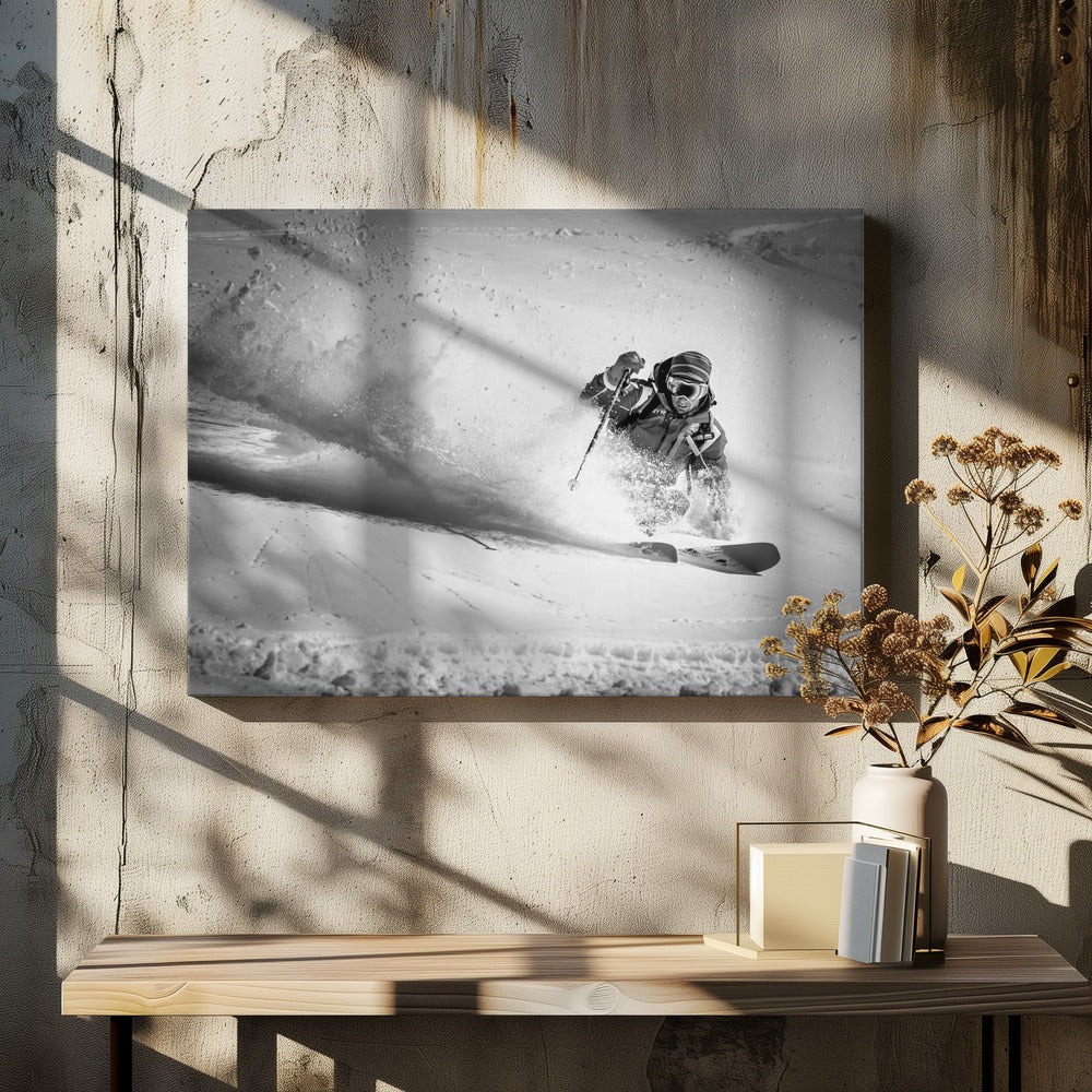 A framed, black and white action shot of a skier making a sharp turn on a snowy slope, sending a large spray of powder into the air. The skier is leaning into the turn, fully kitted out in winter gear including goggles and a beanie. Artwork
