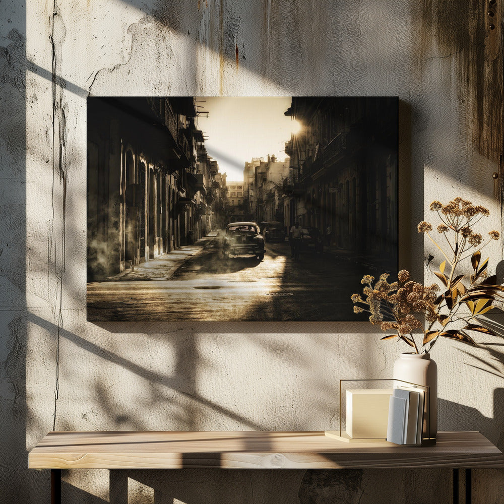 A sepia-toned, atmospheric photograph of a classic car driving down a narrow street in an old city. The sun hangs low, casting long shadows and illuminating smoke or dust in the golden air. Artwork
