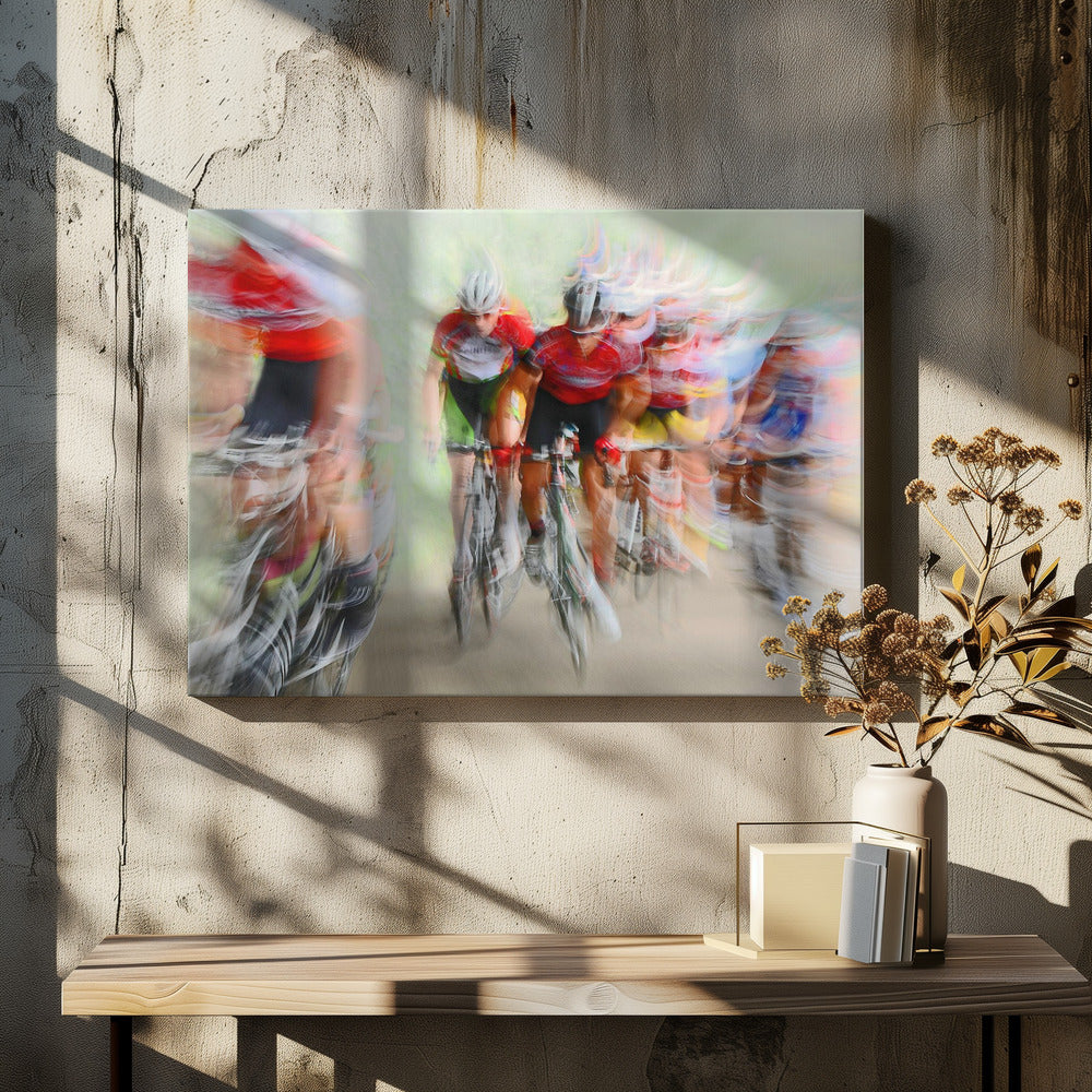An abstract photograph of a group of cyclists in a race, captured with motion blur to create a dynamic sense of speed. The riders' red jerseys and the green background are streaked together, with a silver frame surrounding the image. Artwork