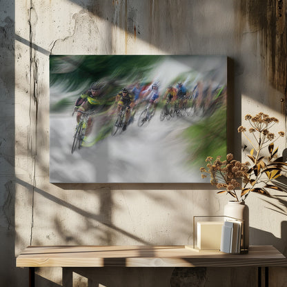 A dynamic, motion-blurred photograph of a group of cyclists in a race, captured with a slow shutter speed to create streaks of color and a sense of high speed. The lead cyclist in a yellow and black jersey is the most defined figure, leaning into a turn on a grey road flanked by blurry green foliage. The entire image is enclosed in a silver frame. Decor