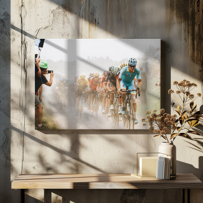 A framed photograph of a peloton of professional cyclists racing down a dusty dirt road. The lead cyclist is in sharp focus, wearing a bright turquoise uniform and a helmet, with other racers in yellow and red jerseys blurred behind him. A spectator on the left is taking a photo with a smartphone. Poster