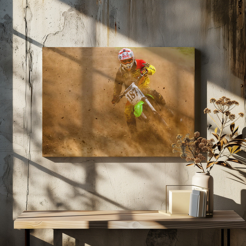 An action shot of a motocross rider in full red and yellow gear, speeding through a dirt track and kicking up a large cloud of brown dust and debris. Print