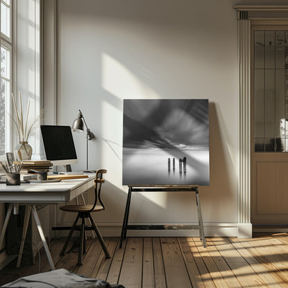 A framed, square, black and white long-exposure photograph of a minimalist seascape. Four dark wooden pilings emerge from still, misty water under a dramatic, streaked sky of dark clouds. Wall Art