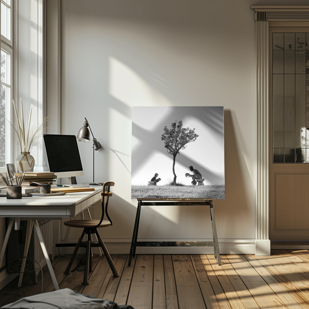 A framed, black and white photograph depicting a surreal scene of a man and a child sitting on toilets in an open grassy field under a single tree, both wearing hats and reading. Print