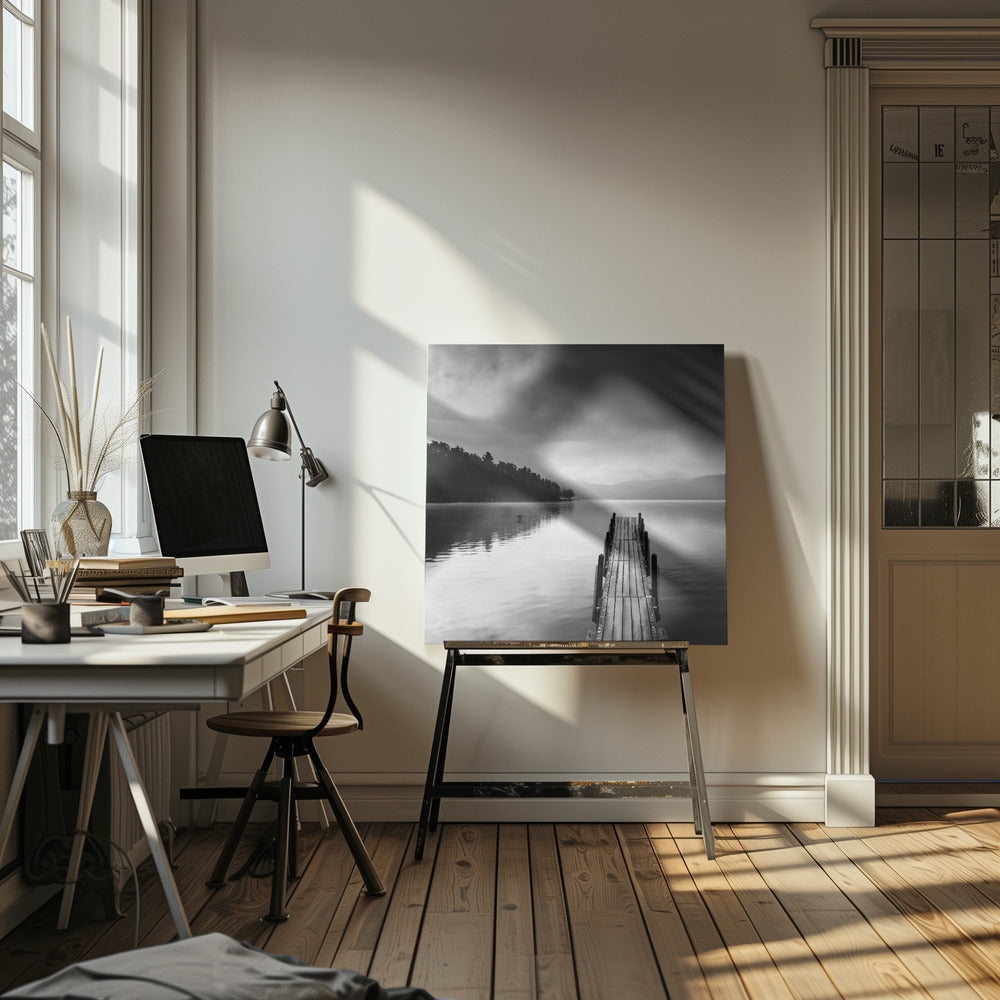 A framed, moody black and white photograph of a wooden pier extending into a calm lake under a cloudy sky, with a forested shoreline and distant mountains in the background. Poster