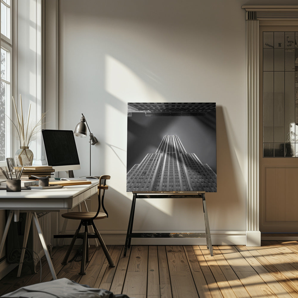 A dramatic, low-angle, black and white photograph of the Empire State Building, looking up from the street. The building's Art Deco lines stretch towards a dark grey sky, with another building visible at the very top of the frame, all enclosed in a light brown wood frame. Wall Art