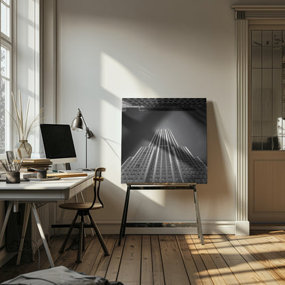 A dramatic, low-angle, black and white photograph of the Empire State Building, looking up from the street. The building's Art Deco lines stretch towards a dark grey sky, with another building visible at the very top of the frame, all enclosed in a light brown wood frame. Wall Art