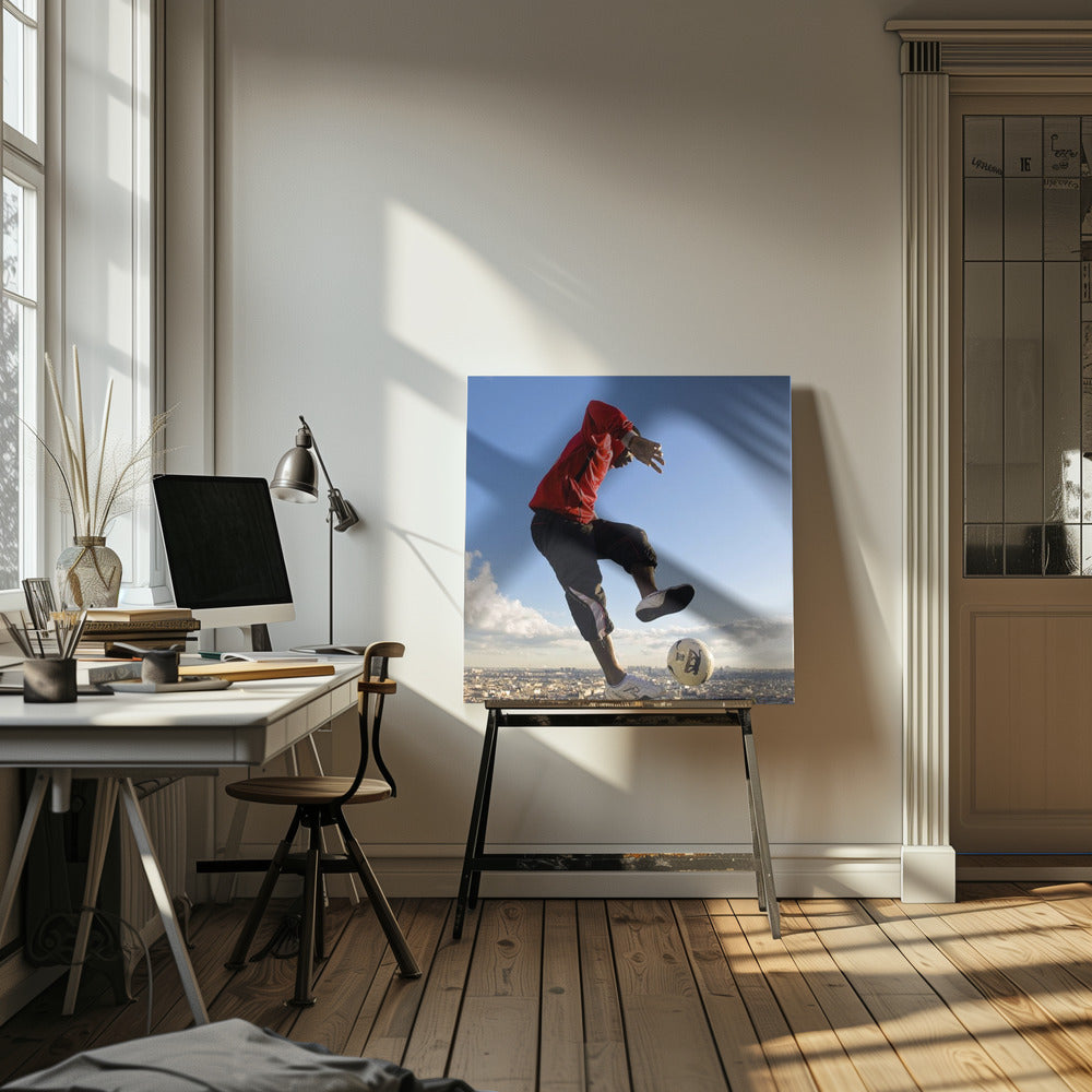 A dynamic low-angle shot of a person in a red jacket and black pants skillfully juggling a soccer ball, suspended in mid-air high above a sprawling city skyline under a clear blue sky, all enclosed within a light wood frame. Artwork