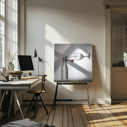 A conceptual photograph in a light wood frame depicting water pouring horizontally from an open swing-top glass bottle into a floating, sideways wine glass against a simple gray background, capturing the liquid in mid-air. Print