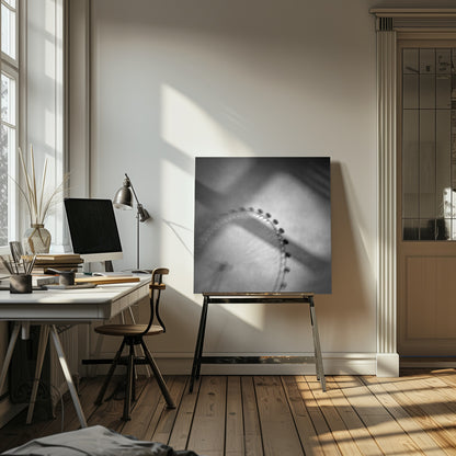 A moody, black and white long-exposure photograph of a large Ferris wheel, creating a soft, blurry effect of its rotation against a grainy gray sky. The artwork is presented in a simple, light wood frame. Poster