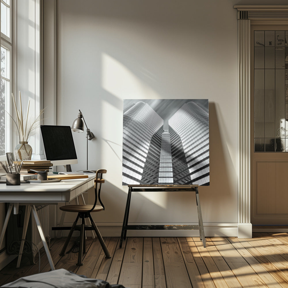 A low-angle, symmetrical black and white photograph of a modern glass skyscraper. The two towers of the building converge towards the center, creating a V-shape against a sky with motion-blurred clouds. The photo is enclosed in a light-colored wooden frame. Print