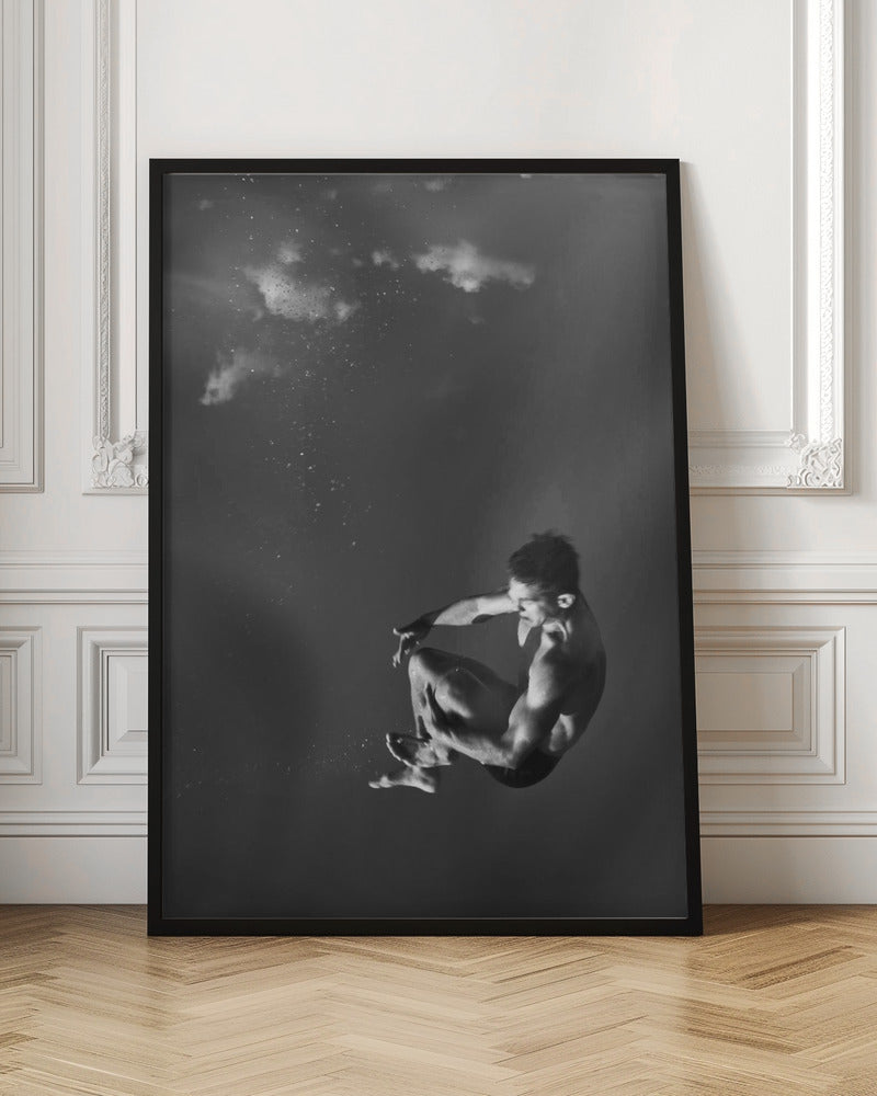 A dramatic black and white photograph of a male diver suspended mid-air in a tuck position. The background is a dark, atmospheric gray, with what appears to be clouds and bubbles, giving the impression of being underwater or in a vast, empty space. The lighting highlights the athlete's muscular physique. Artwork