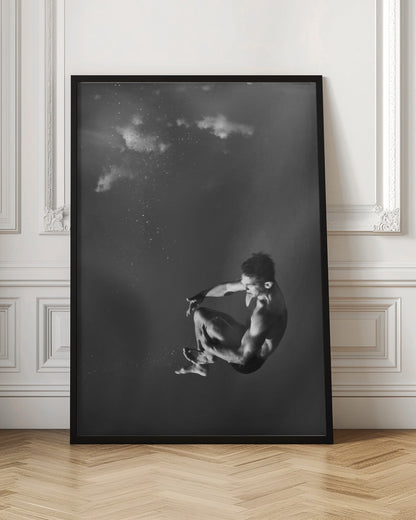A dramatic black and white photograph of a male diver suspended mid-air in a tuck position. The background is a dark, atmospheric gray, with what appears to be clouds and bubbles, giving the impression of being underwater or in a vast, empty space. The lighting highlights the athlete's muscular physique. Artwork