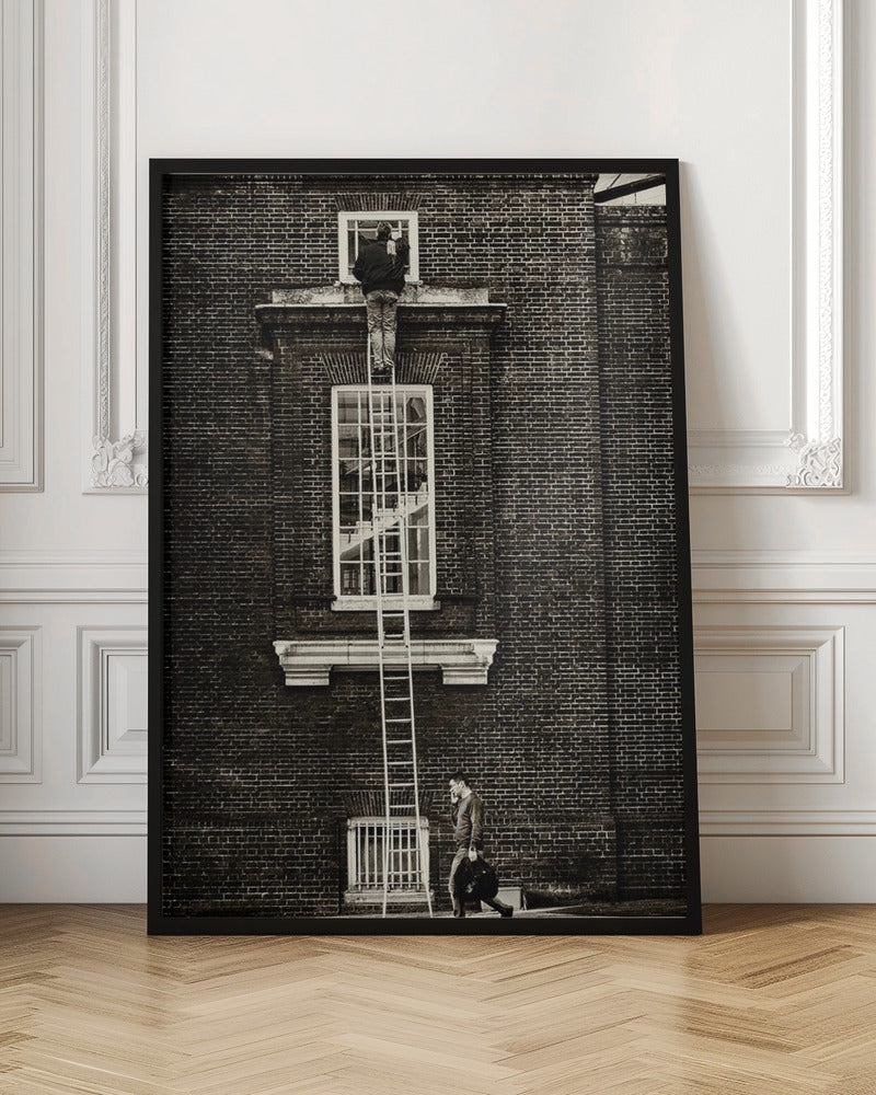 A striking black and white photograph of a man cleaning a small window high up on a brick building, standing precariously at the top of a very long ladder. Below, another man walks past on the street, seemingly unaware of the scene above. Artwork