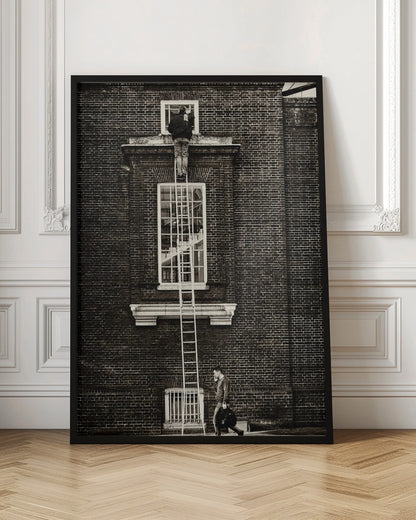 A striking black and white photograph of a man cleaning a small window high up on a brick building, standing precariously at the top of a very long ladder. Below, another man walks past on the street, seemingly unaware of the scene above. Artwork