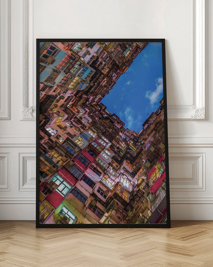 A dramatic worm's-eye view looking up at colorful, densely packed high-rise apartment buildings that create a geometric frame around a patch of deep blue sky. Wall Art