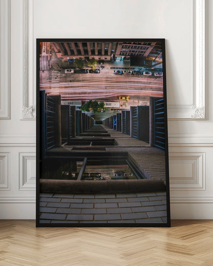 A dizzying bird's-eye view looking straight down the side of a skyscraper into a busy city street at night, with long exposure light trails from traffic creating streaks of red and white below. Wall Art
