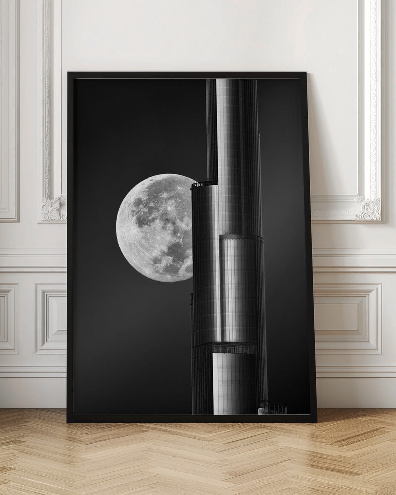 A dramatic black and white photograph of a massive full moon positioned next to a modern, towering skyscraper. The high-contrast image creates a striking juxtaposition between the natural celestial body and the man-made architectural marvel against a dark night sky. Poster
