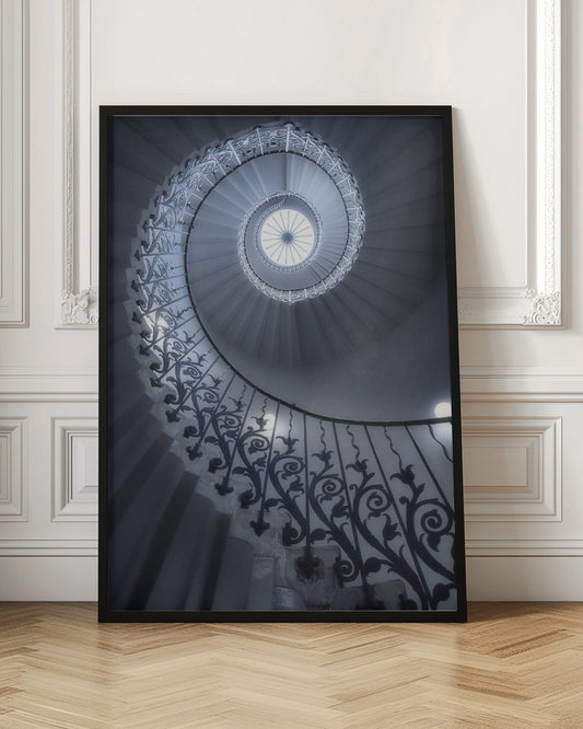 A dramatic low-angle view looking up a majestic spiral staircase, its ornate black wrought iron railings creating a dark, intricate pattern against the cool-toned white steps that wind towards a circular skylight at the apex. Decor