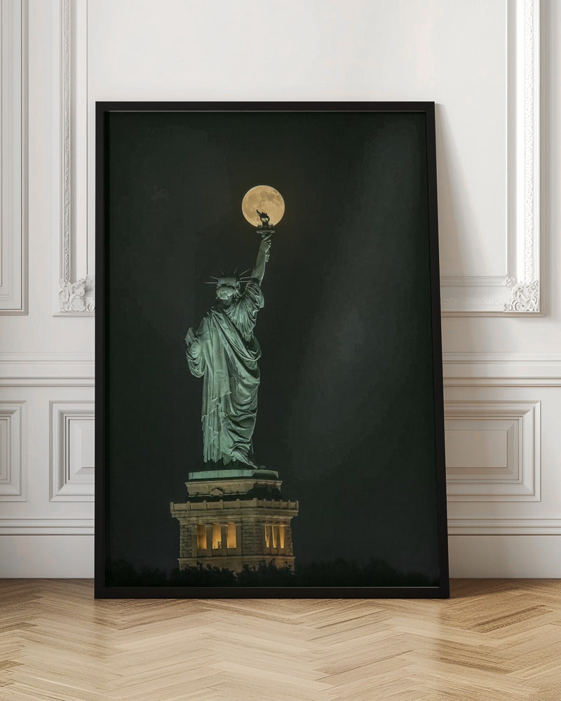 A striking night photograph of the Statue of Liberty, where a large, full yellow moon is perfectly aligned behind the torch, creating the illusion that the statue is holding up the moon. Artwork