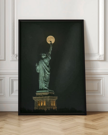 A striking night photograph of the Statue of Liberty, where a large, full yellow moon is perfectly aligned behind the torch, creating the illusion that the statue is holding up the moon. Artwork