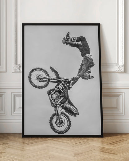A dynamic black and white action shot of a freestyle motocross rider performing a handstand on the handlebars of their dirt bike mid-air. The bike is nearly vertical against a plain white sky, capturing a moment of extreme athleticism and balance. Poster