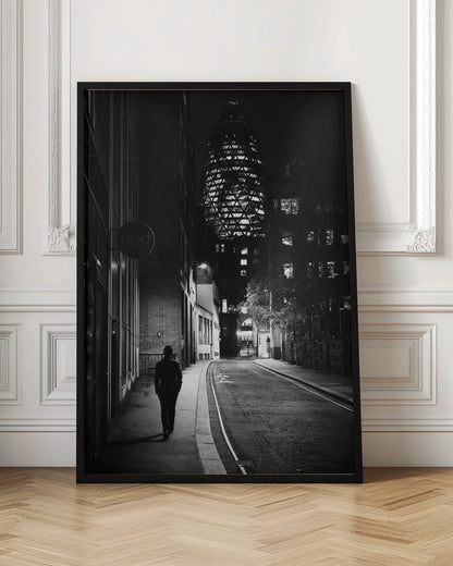 A moody black and white photograph of a person walking away down a narrow, deserted city street at night. In the background, the iconic Gherkin building in London is brightly lit against the dark sky. Wall Art