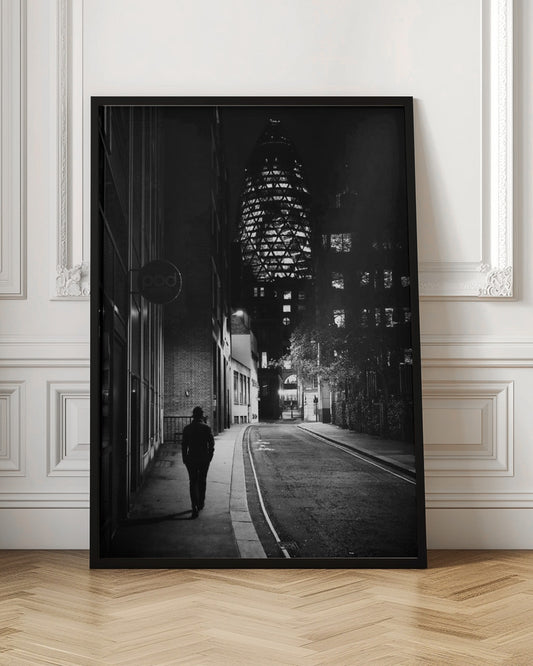 A moody black and white photograph of a person walking away down a narrow, deserted city street at night. In the background, the iconic Gherkin building in London is brightly lit against the dark sky. Wall Art