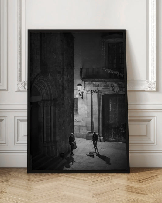 A high-angle, black and white photograph of a street musician playing a saxophone for a lone listener in a narrow stone alley at night. The scene is illuminated by an ornate streetlamp, casting long shadows on the cobblestone ground. Wall Art