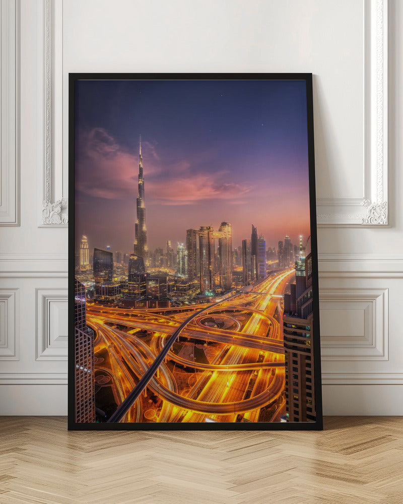A stunning aerial photograph of the Dubai skyline at dusk, featuring the illuminated Burj Khalifa against a purple and pink sunset sky. In the foreground, complex highway interchanges are aglow with the golden-orange light trails of moving traffic, creating a sense of vibrant energy. Poster