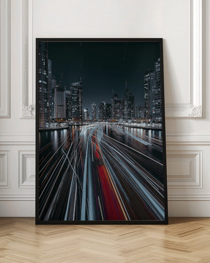 A dynamic long-exposure photograph of a bustling city marina at night. In the foreground, vibrant streaks of red and white light from moving boats cut across the dark water. In the background, a modern skyline of illuminated skyscrapers stands against a dark night sky, creating a futuristic and energetic scene. Poster