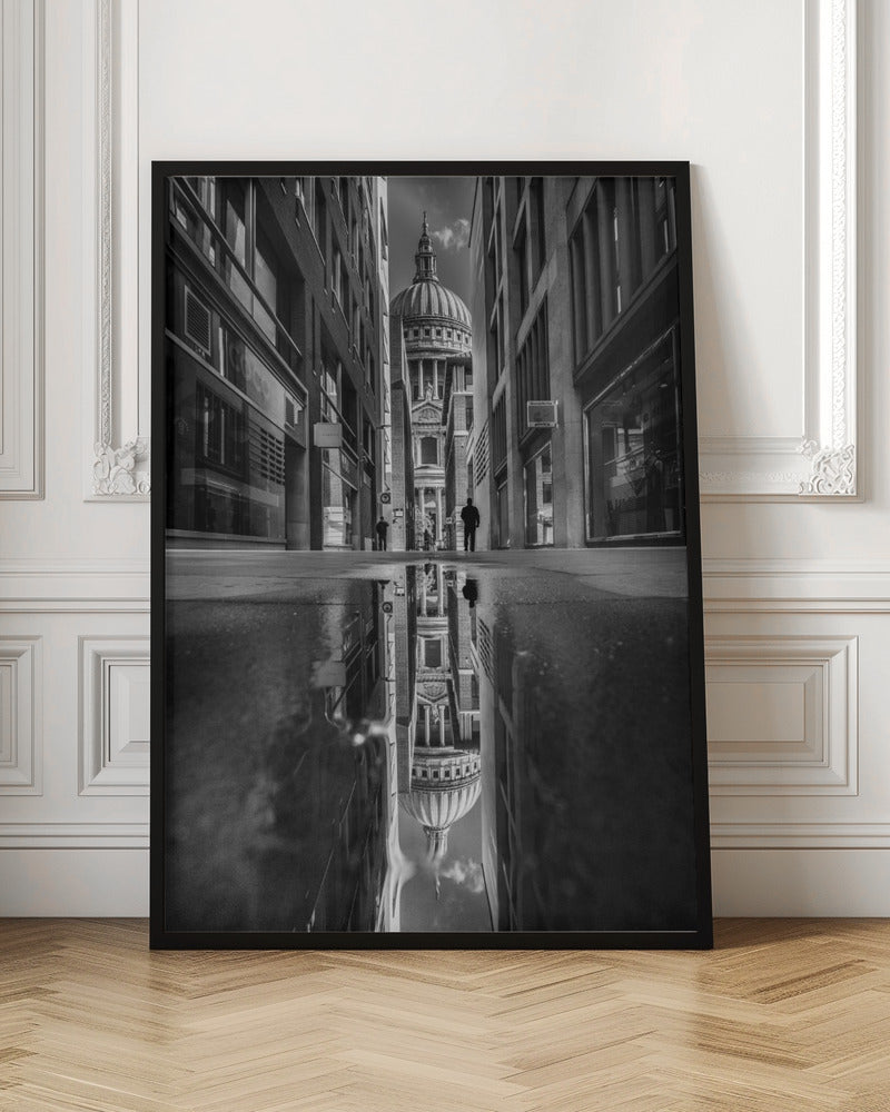 A dramatic black and white photograph taken from a low angle on a narrow city street, perfectly framing St. Paul's Cathedral in the distance. The foreground is dominated by a large puddle, which creates a stunning, clear reflection of the entire scene, including the cathedral, buildings, and sky. Print