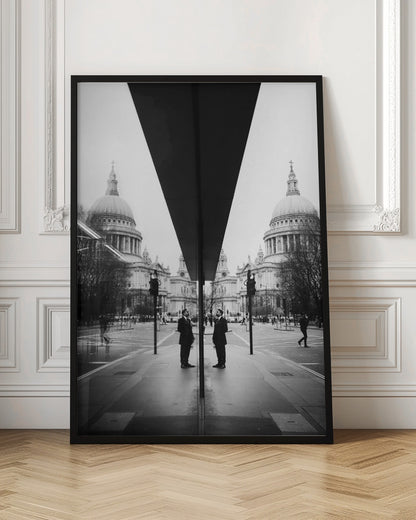 A surreal black and white photograph capturing a symmetrical reflection of a city scene, with St. Paul's Cathedral prominently featured on both sides. A dark, V-shaped reflection from a building divides the image vertically. In the foreground, the reflection of two men in dark suits standing on the sidewalk adds a human element to the grand architectural view. Decor