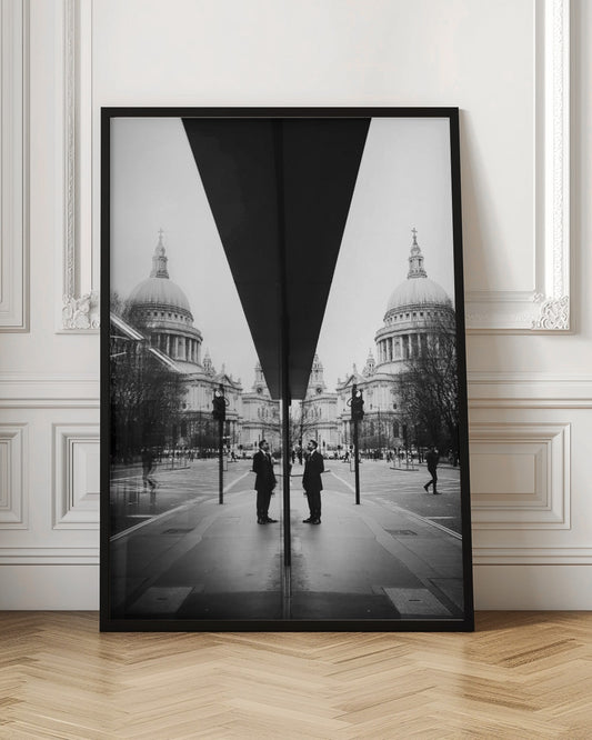 A surreal black and white photograph capturing a symmetrical reflection of a city scene, with St. Paul's Cathedral prominently featured on both sides. A dark, V-shaped reflection from a building divides the image vertically. In the foreground, the reflection of two men in dark suits standing on the sidewalk adds a human element to the grand architectural view. Decor