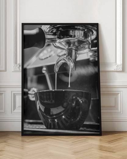 A close-up, black and white photograph of an espresso machine pouring two streams of fresh coffee from a chrome portafilter into a dark, glossy cup. Print