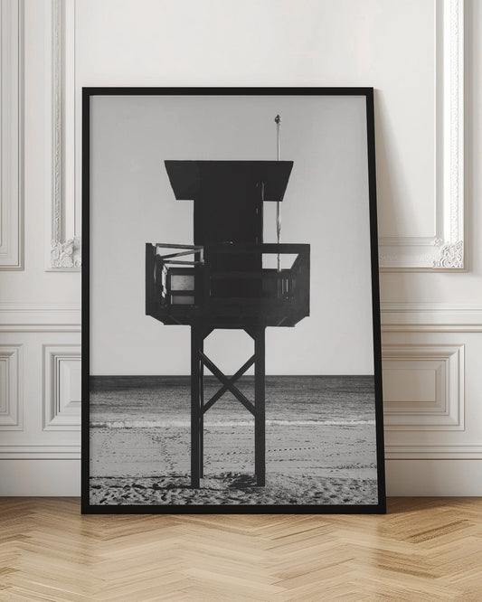 A high-contrast, black and white photograph of a silhouetted lifeguard tower standing on a sandy beach. The tower is centrally framed against a bright, empty sky, with the ocean and horizon visible in the background. Wall Art