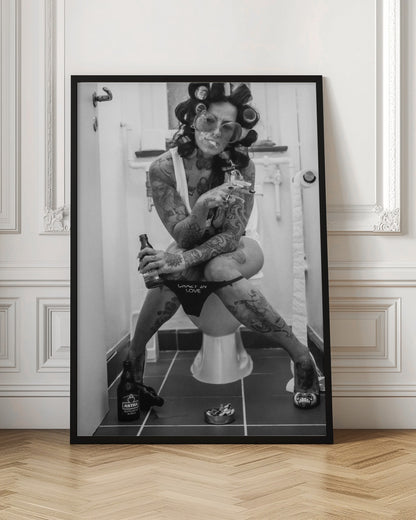 A black and white photo of a heavily tattooed woman with her hair in rollers sitting on a toilet. She wears large sunglasses, smokes a cigarette, holds a beer bottle, and has on black underwear that says 'CRAZY IN LOVE'. An ashtray and another beer bottle are on the floor. Artwork