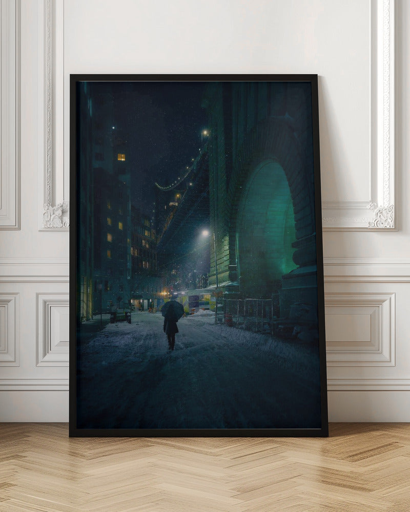 A lone person holding an umbrella walks down a snow-covered street at night, dwarfed by the massive, green-lit stone archway of the Brooklyn Bridge as snow falls around them. Print