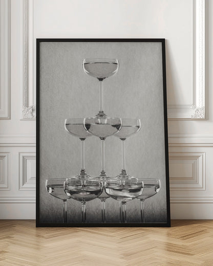 A classic black and white photograph of a champagne tower, with coupe glasses stacked in a pyramid. The glasses are filled with bubbly liquid, and the composition is set against a textured light gray background and enclosed in a black frame. Poster