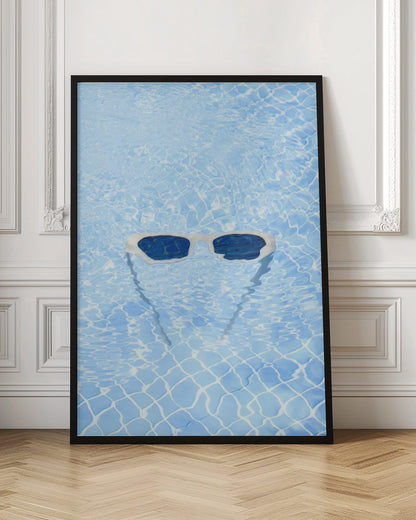 A pair of white-framed sunglasses with dark lenses floats on the surface of a bright blue swimming pool. The rippling water distorts the view of the tiled pool floor, and the sunglasses cast a faint shadow underneath. Print
