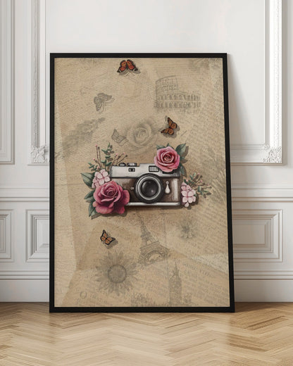 A vintage-style collage art piece in a black frame. The central focus is a retro camera adorned with pink and magenta roses and green leaves. The background is a sepia-toned collage of old newspaper or book pages, with faint illustrations of European landmarks like the Colosseum and the Eiffel Tower, along with butterflies and flowers. Poster