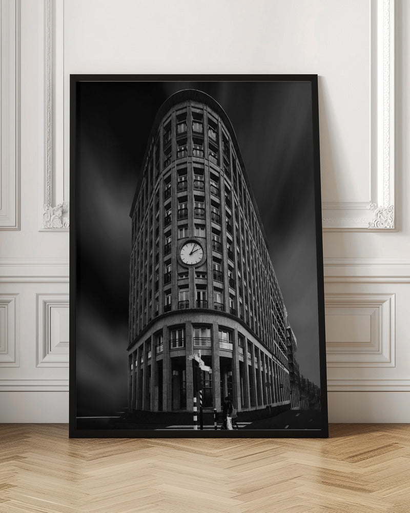 A dramatic low-angle, black and white photograph of a large, curved corner building with a prominent clock on its facade. The sky is dark with a motion blur effect, making the building appear grand and imposing. Artwork