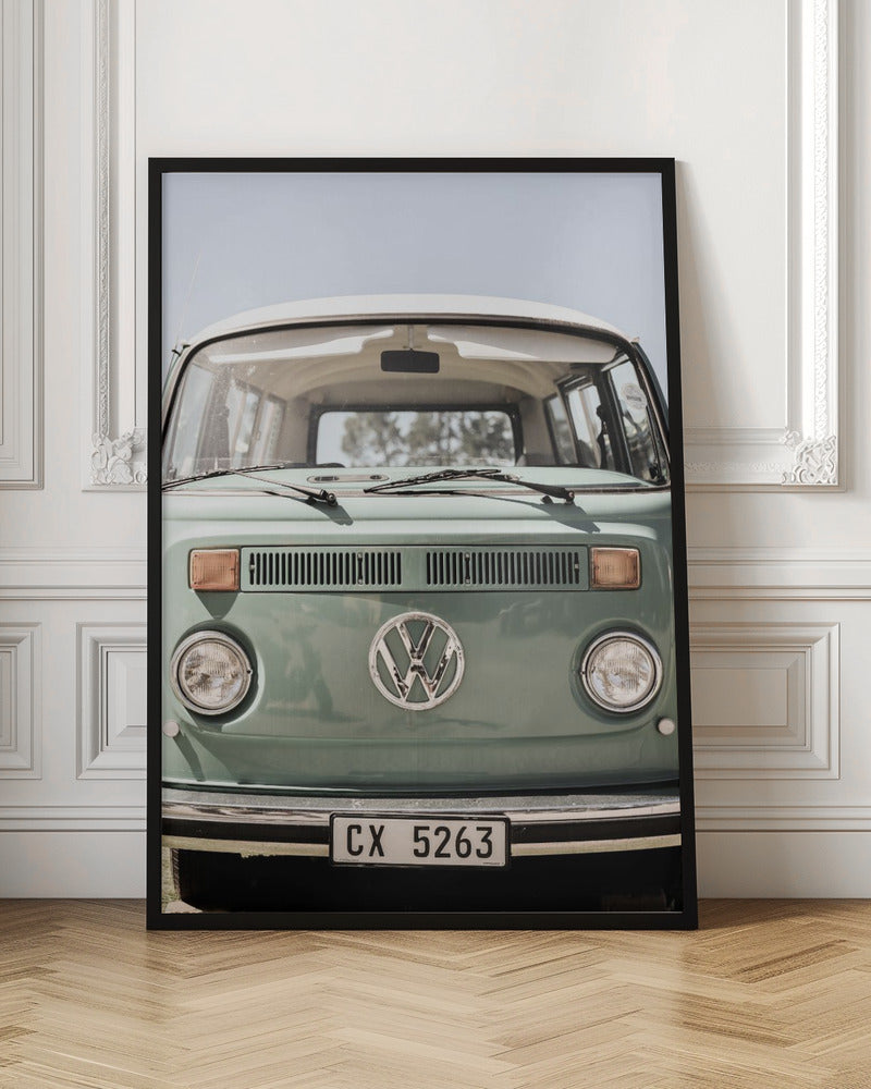 A close-up front view of a vintage sage green Volkswagen bus with a white roof. The iconic VW logo is on the front, with round headlights and a European license plate, set against a pale blue sky. Print