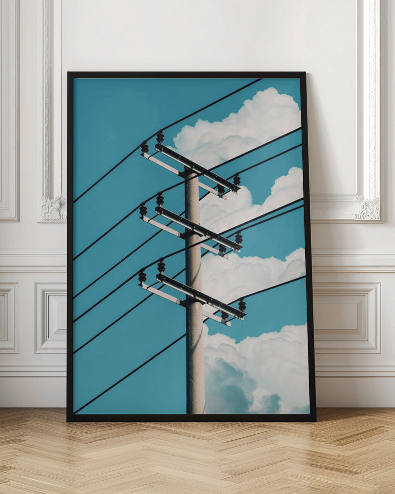 A low-angle photograph of a concrete utility pole with black power lines stretching diagonally across the frame against a vibrant blue sky with fluffy white clouds. Decor