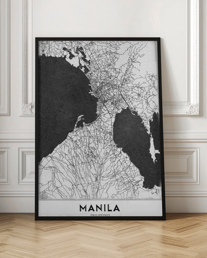 A minimalist black and white map of Manila, Philippines, presented in a black frame. The map showcases the city's intricate road network in black lines on a white landmass, contrasted against textured black bodies of water. The word 'MANILA' is printed in a bold, black sans-serif font at the bottom of the poster. Decor