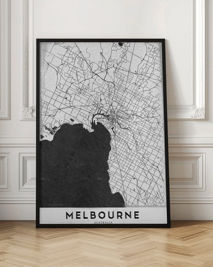A minimalist black and white map of Melbourne, Australia, presented in a black frame. The city's road network is depicted with fine black lines on a textured white background, while the adjacent bay is shown in solid, textured black. The name 'MELBOURNE' is written in a bold, black font at the bottom. Poster