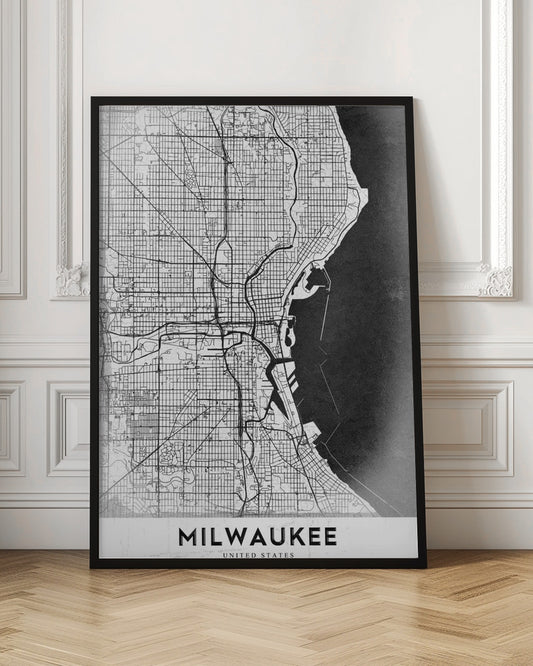A minimalist, black and white street map of Milwaukee, displayed in a black frame. The map details the city's grid system, major roads, and waterways against a textured background, with the word 'MILWAUKEE' in a bold, sans-serif font at the bottom. Poster