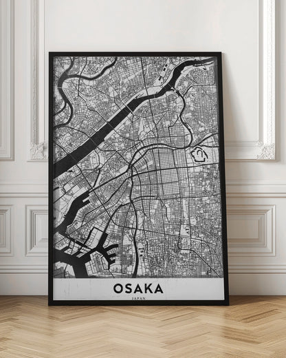 A framed black and white map of Osaka, Japan. The map details the city's streets, blocks, and rivers in a modern, graphic style. At the bottom, a white border contains the word 'OSAKA' in a bold, black, sans-serif font. Print